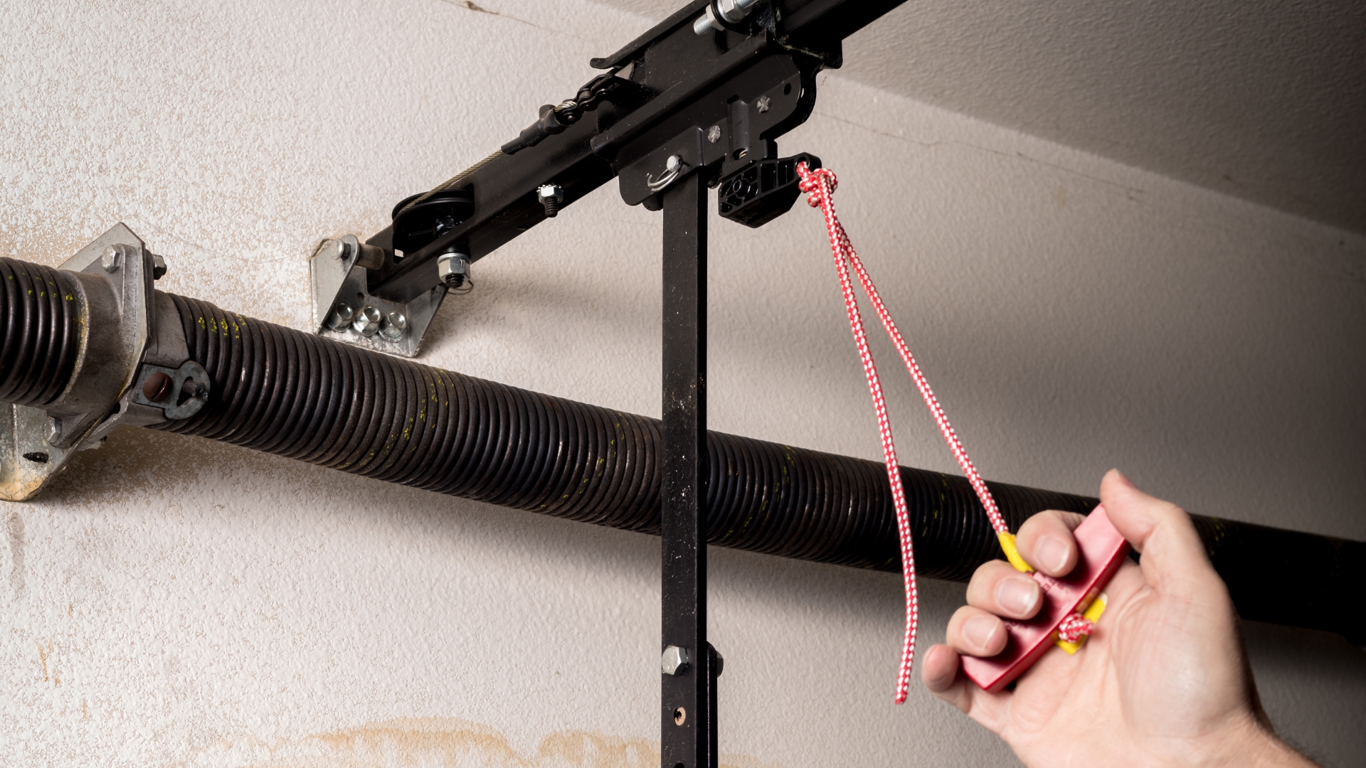 A hand is pulling a red emergency release cord on the garage door opener.